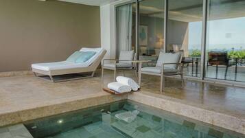A poolside area with lounge chairs, a glass-enclosed balcony, and a view of the landscape.