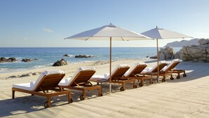 Une plage avec des chaises longues en bois et des parasols blancs.