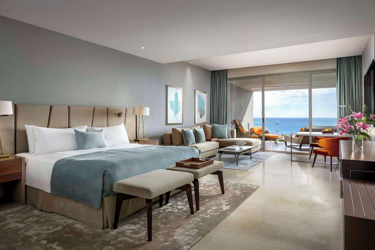 Habitación de hotel moderna con una cama grande, un sofá, un comedor y vista al mar.