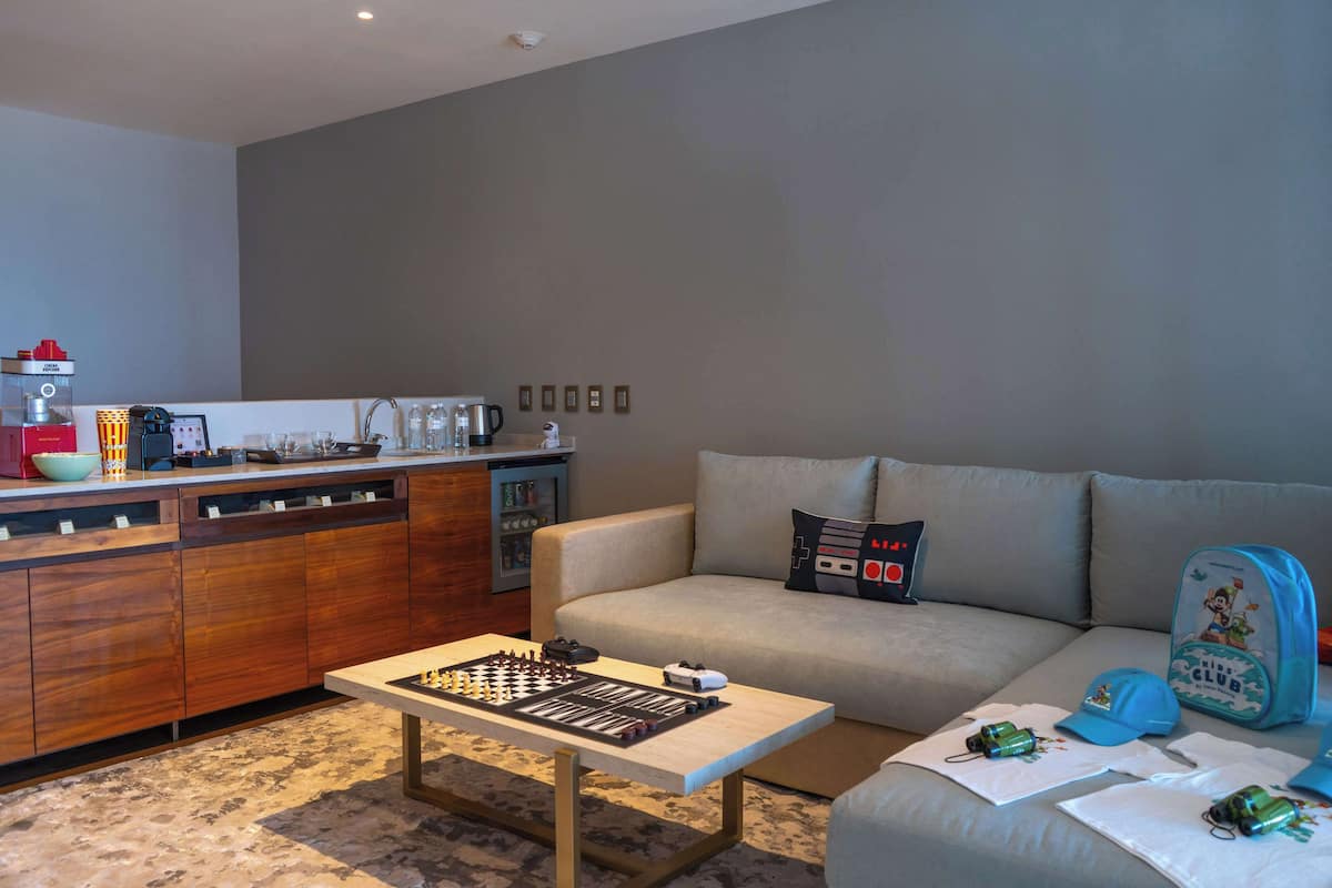 Una sala de estar moderna con un sofá, una mesa de centro y una zona de cocina con lavavajillas y cafetera.
