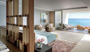 A modern hotel room with a large bed, two armchairs, a sofa, and a balcony with a view of the sea.