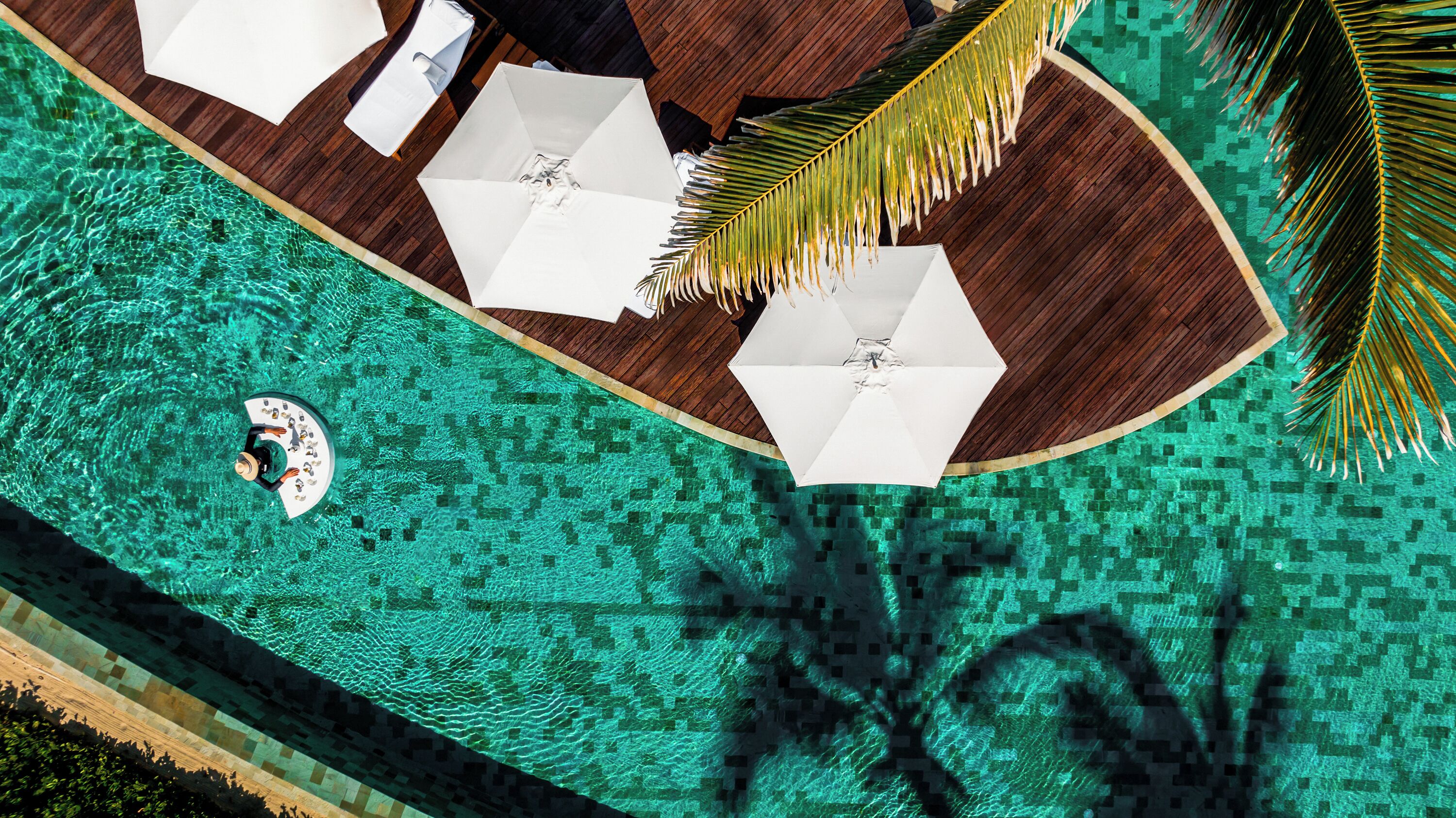 An aerial view of a pool area with a wooden deck, white umbrellas, and lounge chairs.