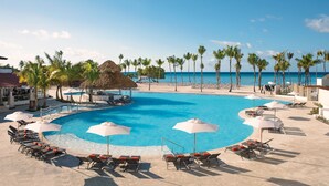 A pool area with lounge chairs and umbrellas, surrounded by palm trees and a view of the ocean. - Dreams Dominicus La Romana - All Inclusive (San Rafael del Yuma)