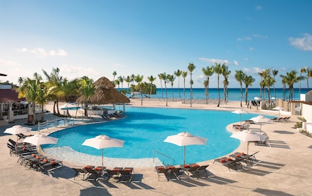 A pool area with lounge chairs and umbrellas, surrounded by palm trees and a view of the ocean.