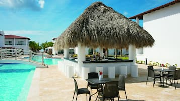 A poolside area with a thatched-roof bar, lounge chairs, and a dining table with chairs.