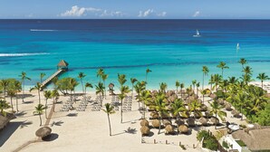 A beach resort with a thatched-roof structure, lounge chairs, and palm trees. - Dreams Dominicus La Romana - All Inclusive (San Rafael del Yuma)