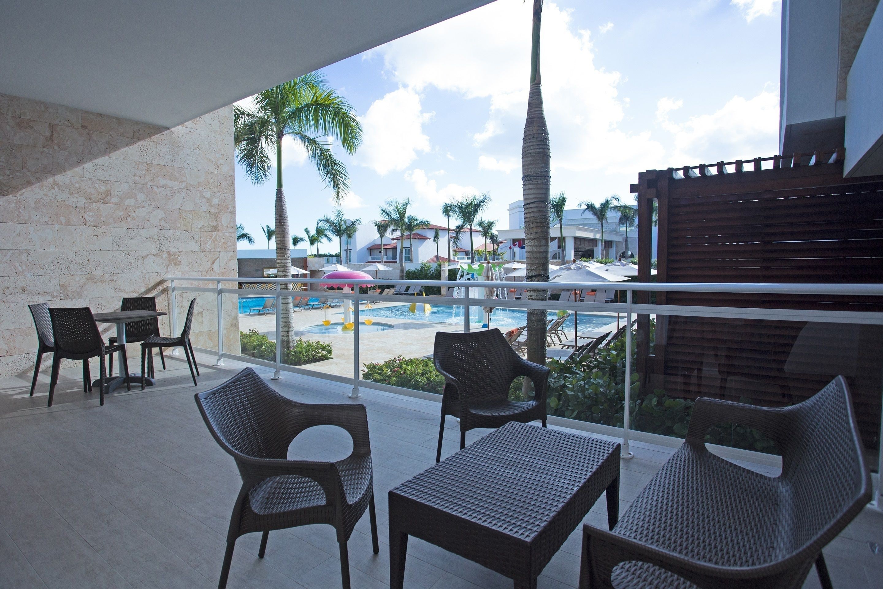 A balcony with wicker furniture, a pool view, and a palm tree.