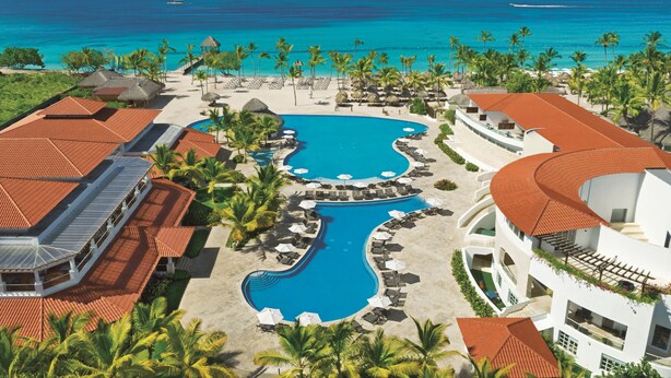 A resort with a central swimming pool, palm trees, and a view of the ocean. - Dreams Dominicus La Romana - All Inclusive (San Rafael del Yuma)