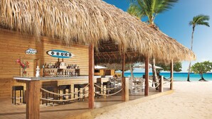 A beachside bar with a thatched roof, wooden furniture, and a view of the ocean. - Dreams Dominicus La Romana - All Inclusive (San Rafael del Yuma)