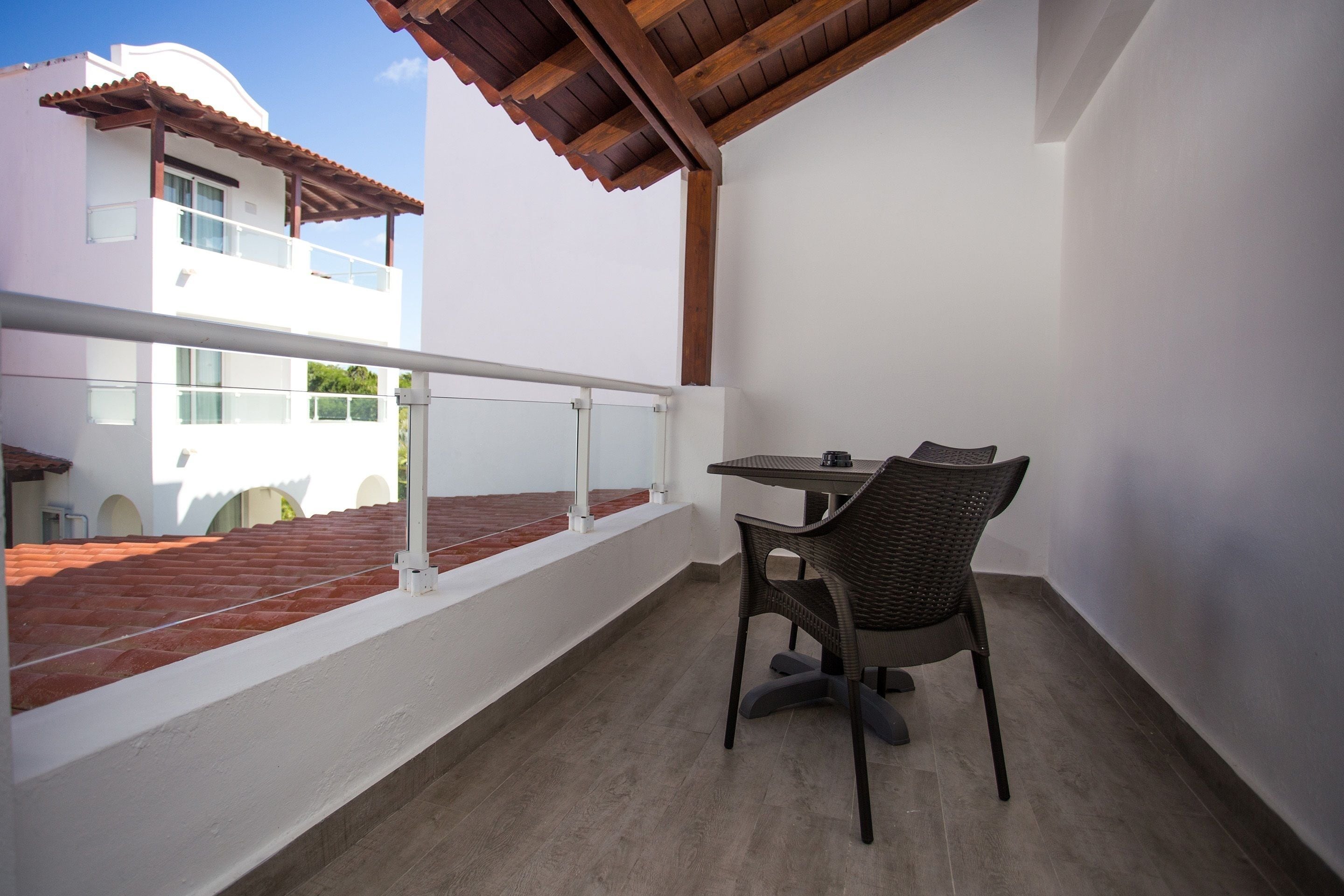 A balcony with a table and chair, a railing, and a view of a building with a red-tiled roof.