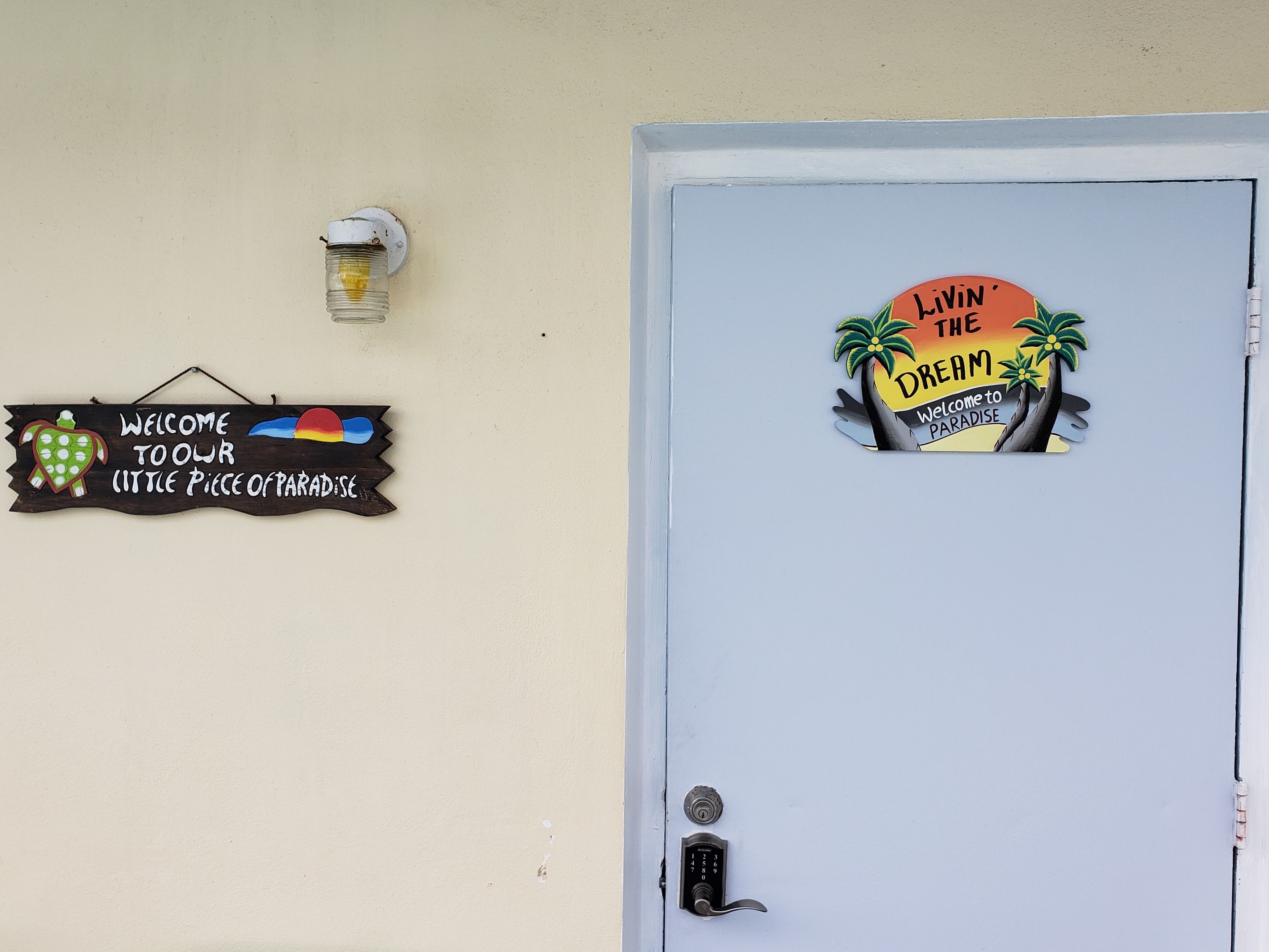 A door with a sign that reads "Welcome to our little piece of paradise" and another sign saying "Livin' the Dream Paradise."