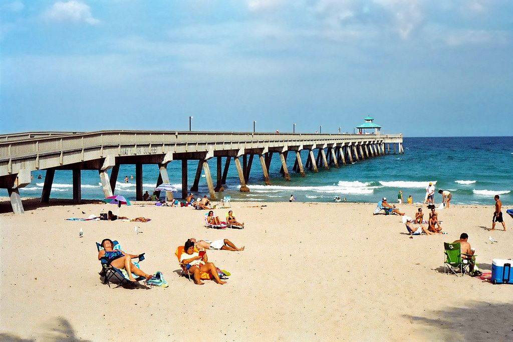 Une jetée qui s’avance dans la mer, avec des gens qui se détendent sur la plage.