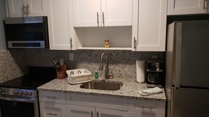 A kitchen with white cabinets, a stainless steel sink, a stove, and a refrigerator. - Ashley Brooke Beach Resort (Deerfield Beach)