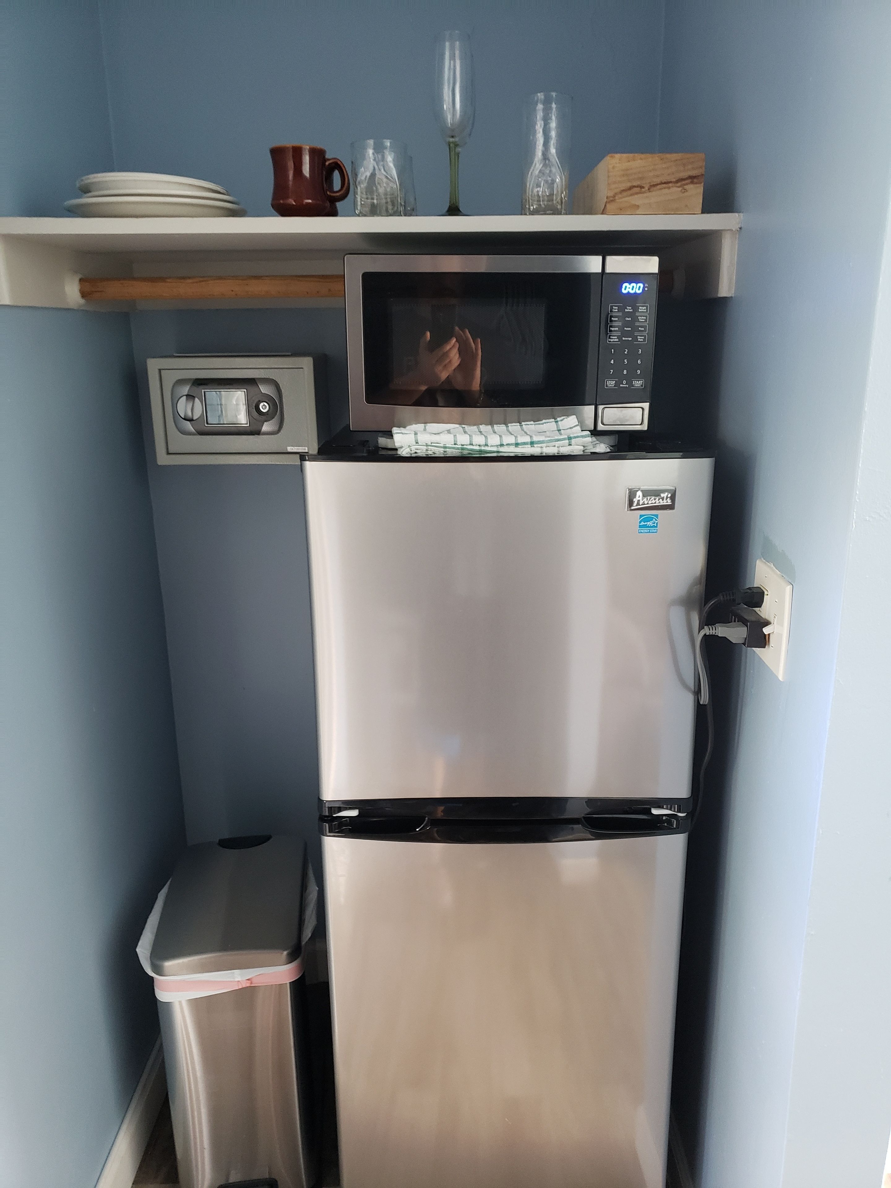 Een compacte keuken met een roestvrijstalen koelkast, een magnetron en een kleine prullenbak.