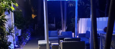 Un patio al aire libre con mobiliario y una pérgola decorada con luces colgantes.