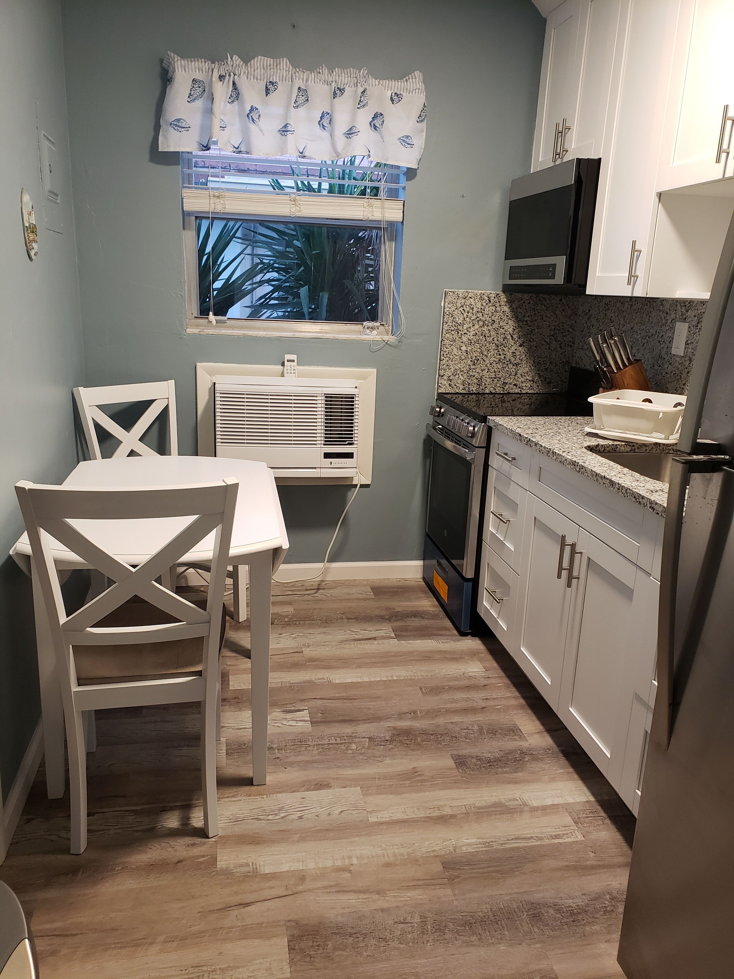 A compact kitchen with white cabinetry, a built-in oven, and a window with a patterned curtain.