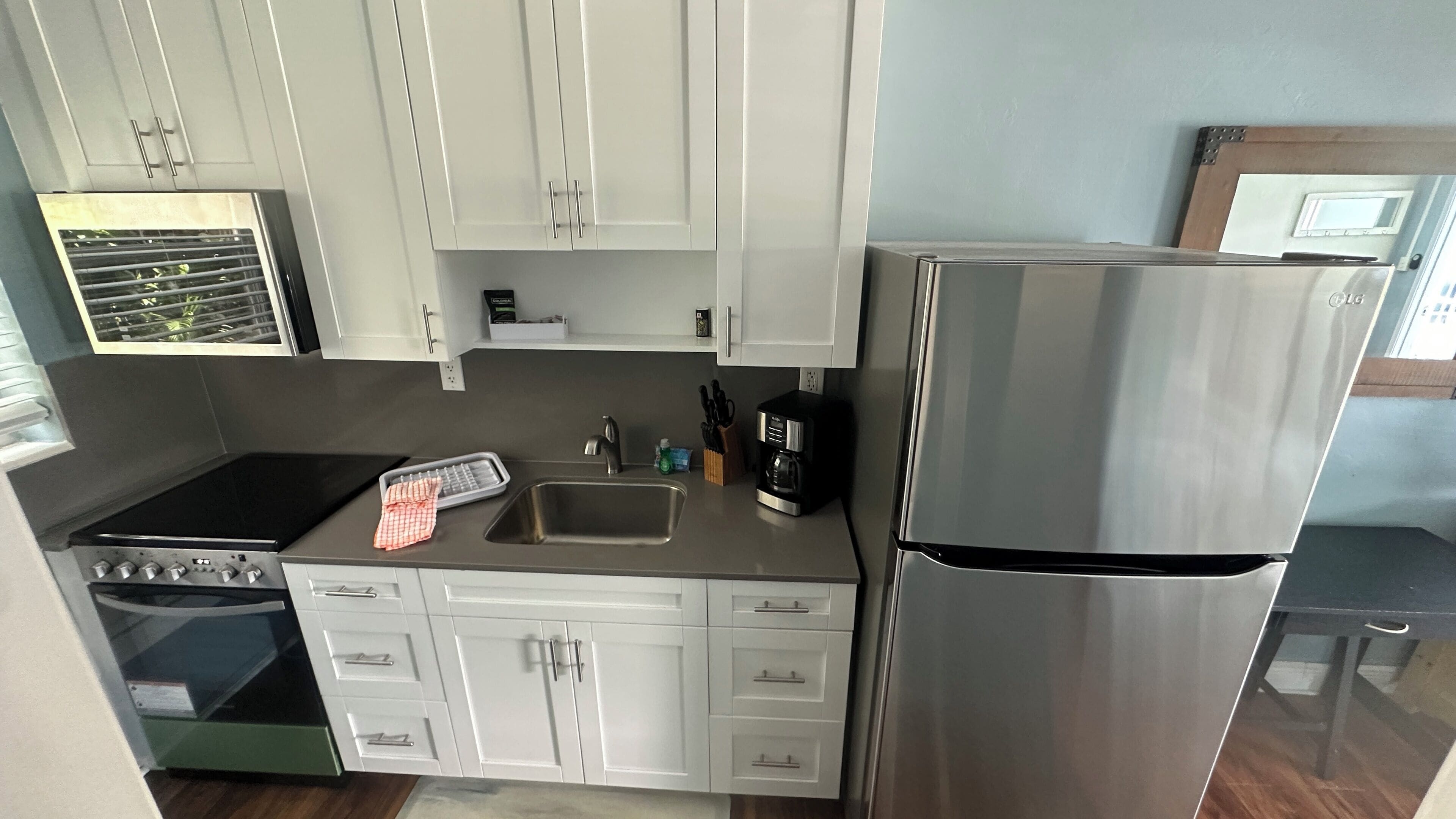 A compact kitchen with white cabinets, a stainless steel refrigerator, a stove, and a sink.
