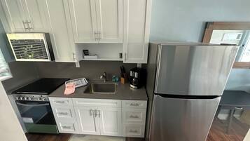 A compact kitchen with white cabinets, a stainless steel refrigerator, a stove, and a sink.