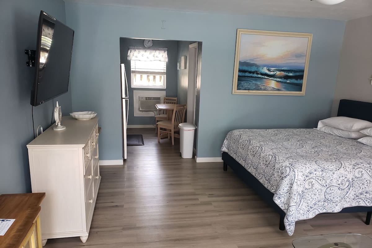 Un dormitorio con cama, cómoda, televisor y un cuadro con una playa.
