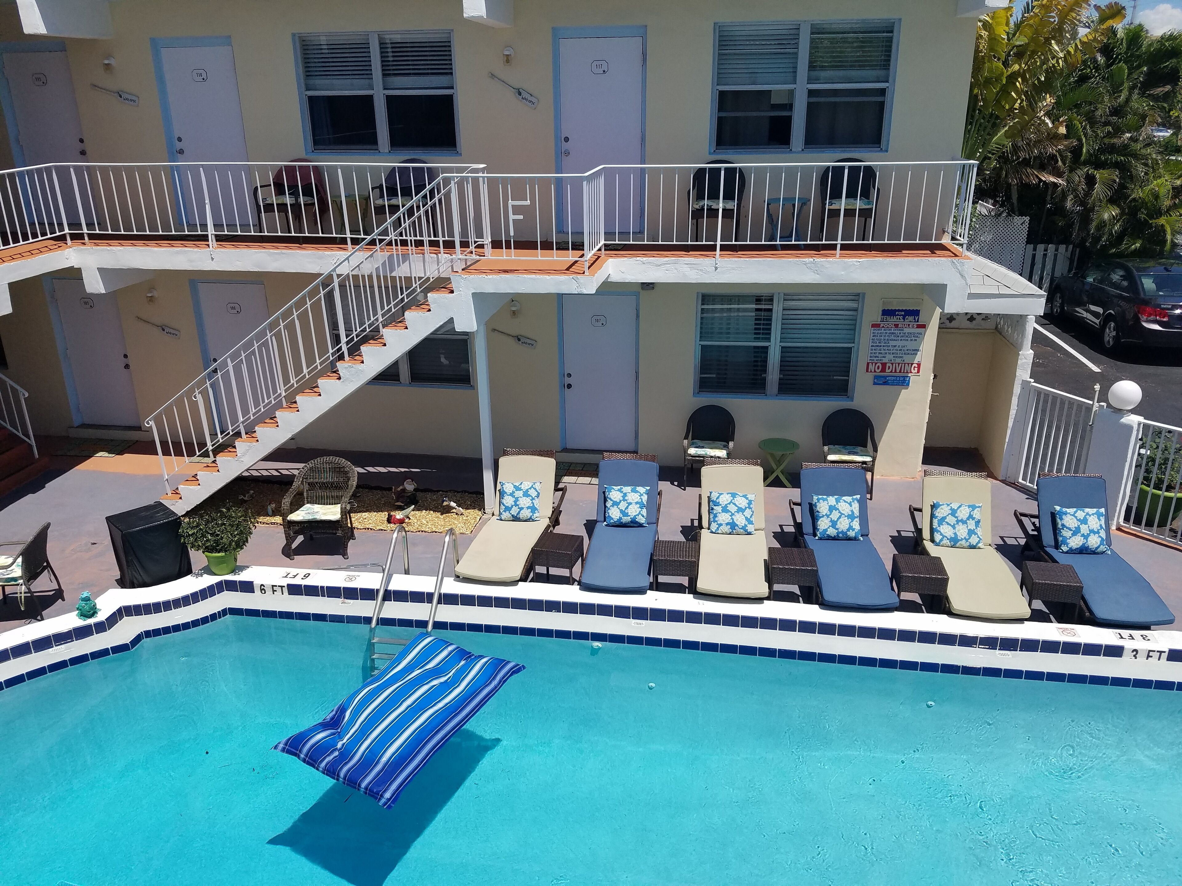 A pool area with lounge chairs and a staircase leading to a balcony.