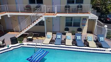 A pool area with lounge chairs and a staircase leading to a balcony.