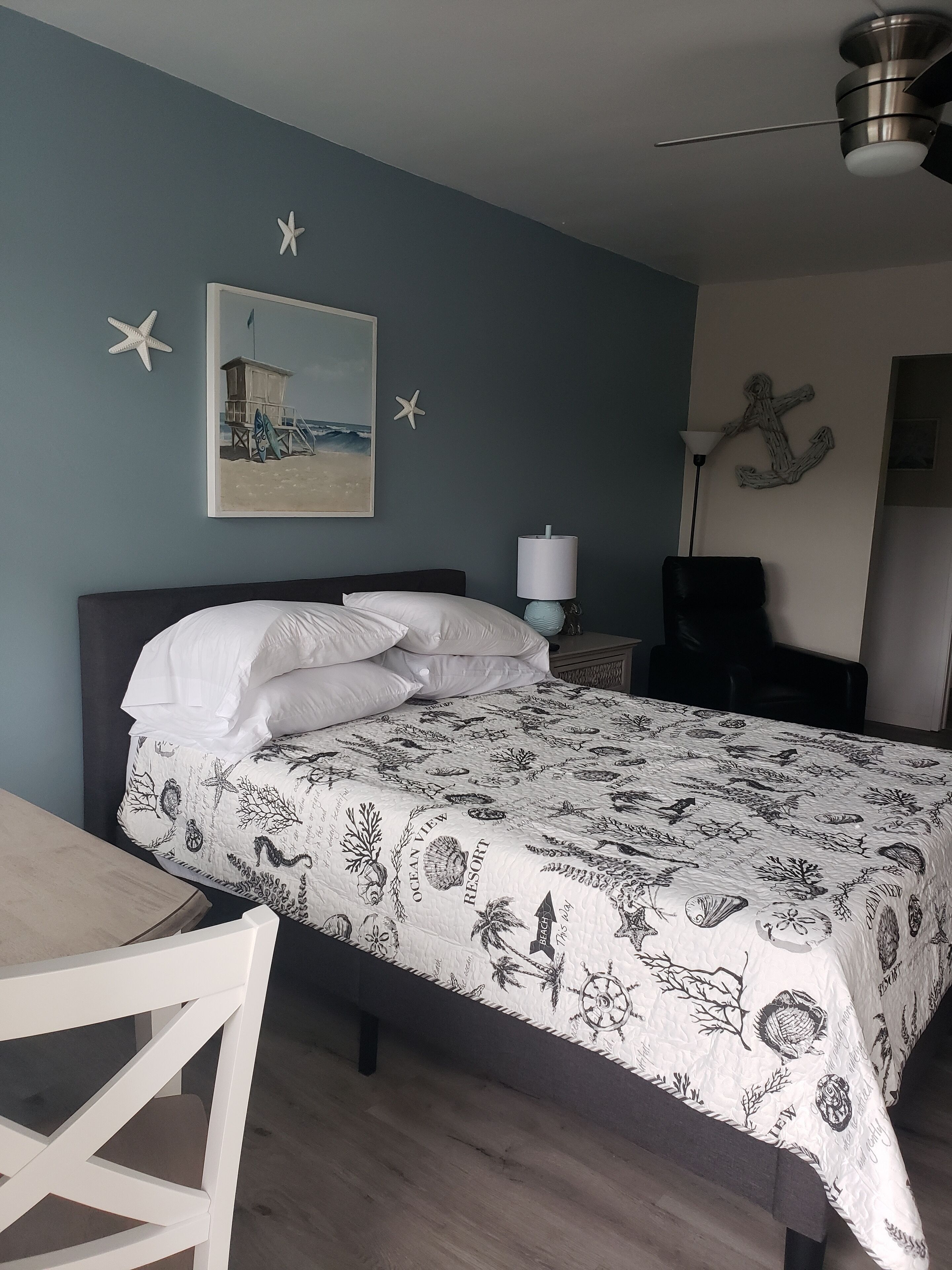 Ein Schlafzimmer mit einem Bett, einem Schreibtisch und einem Stuhl. An der Wand hängt ein Bild und auf dem Schreibtisch steht eine Lampe.
