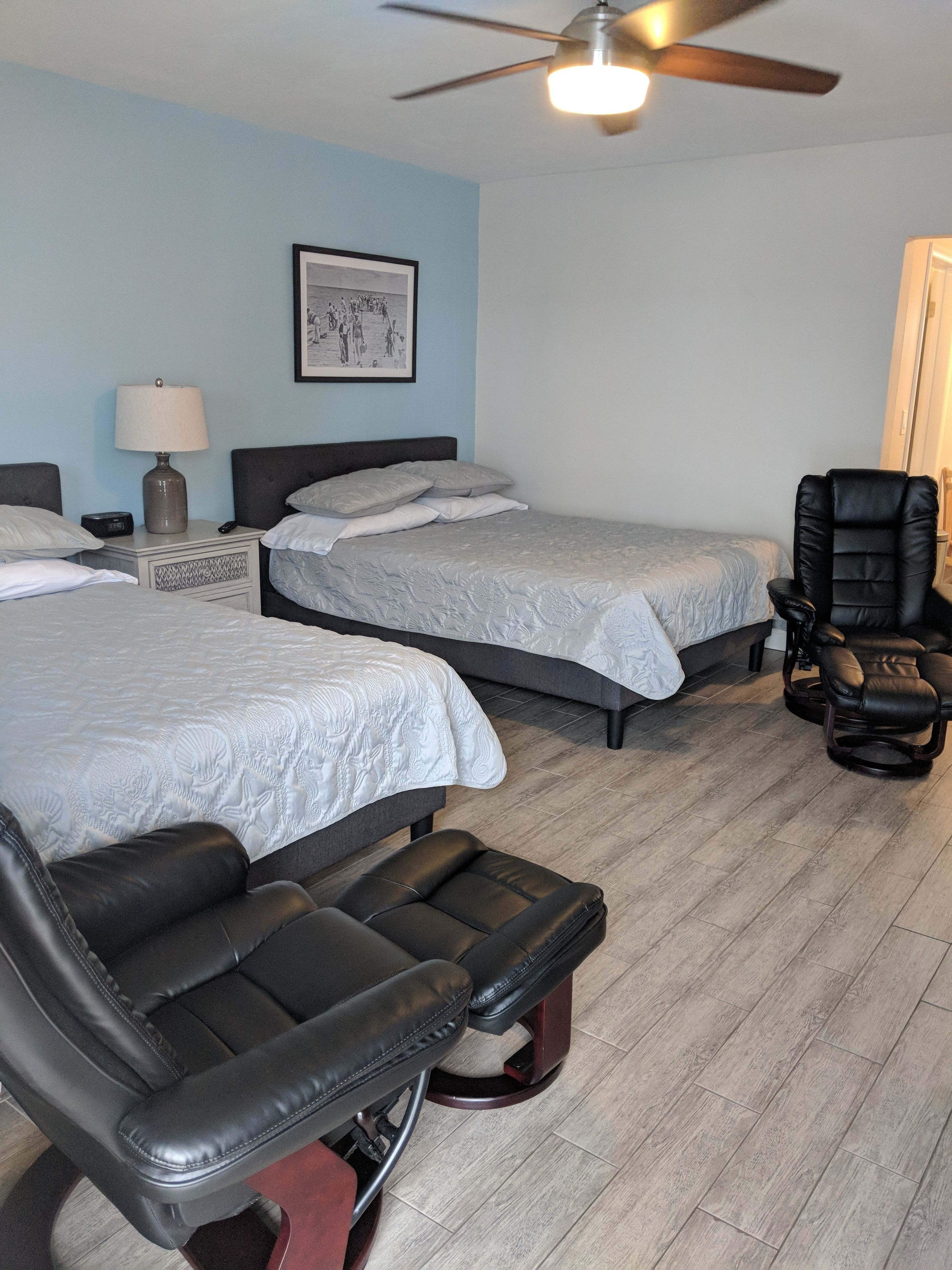 Una habitación de hotel con dos camas, un escritorio con lámpara, una silla y un ventilador de techo.