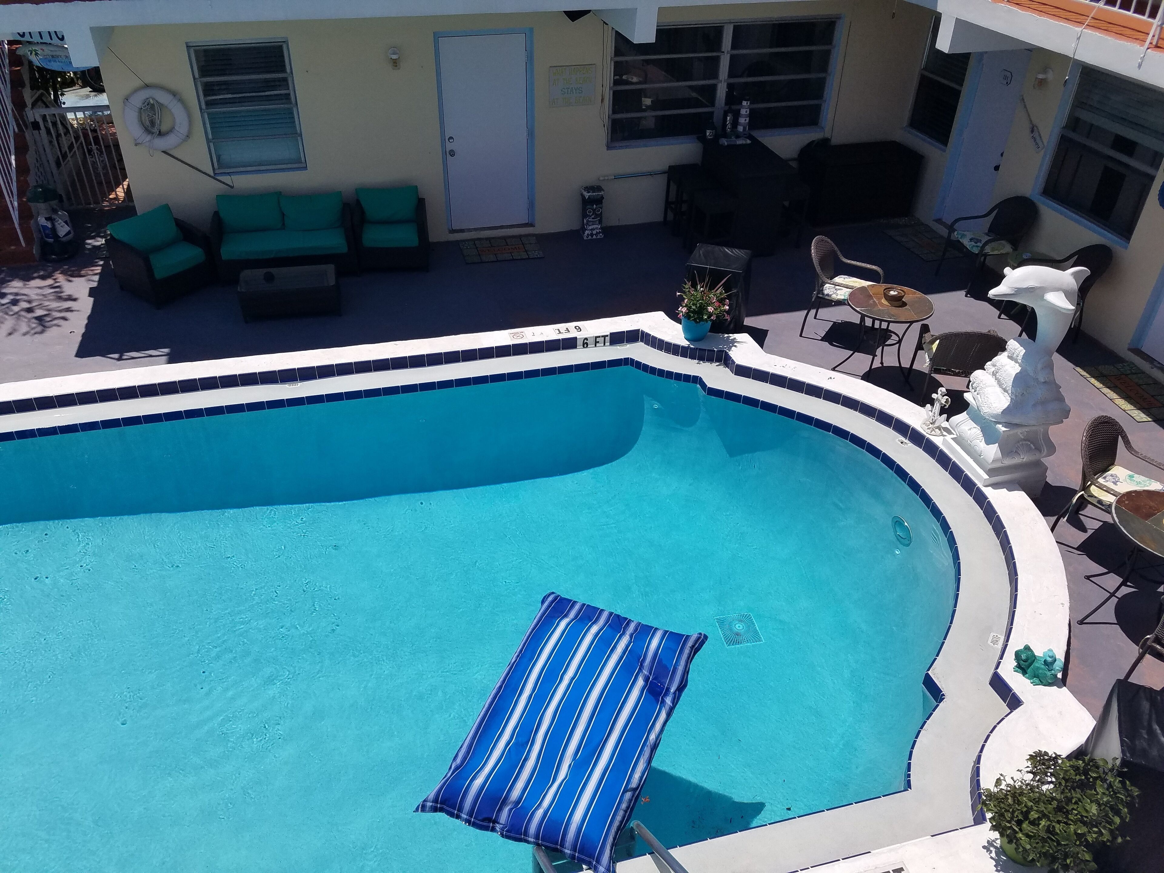 Una piscina con borde de azulejos azules, rodeada de mobiliario exterior que incluye un sofá y sillas.