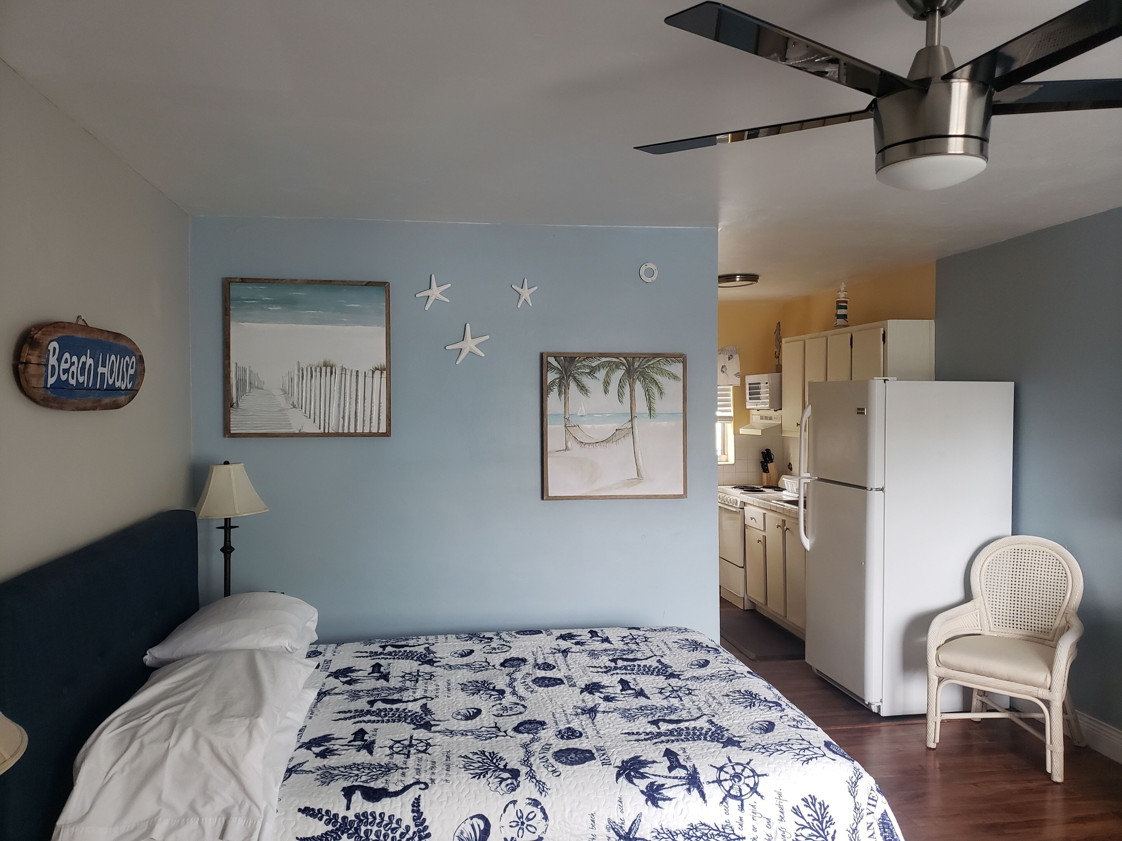 A bedroom with a bed, a ceiling fan, and wall art depicting a beach scene.