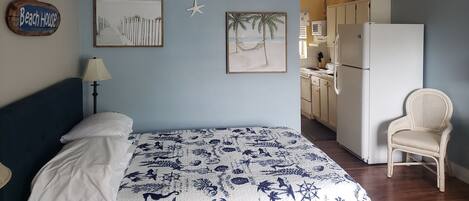 A bedroom with a bed, a ceiling fan, and wall art depicting a beach scene.
