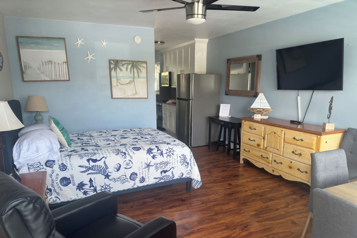 Un dormitorio con cama, escritorio, cómoda, televisor y ventilador de techo.