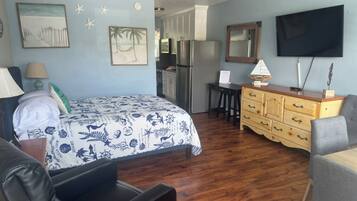 A bedroom with a bed, a desk, a dresser, a TV, and a ceiling fan.