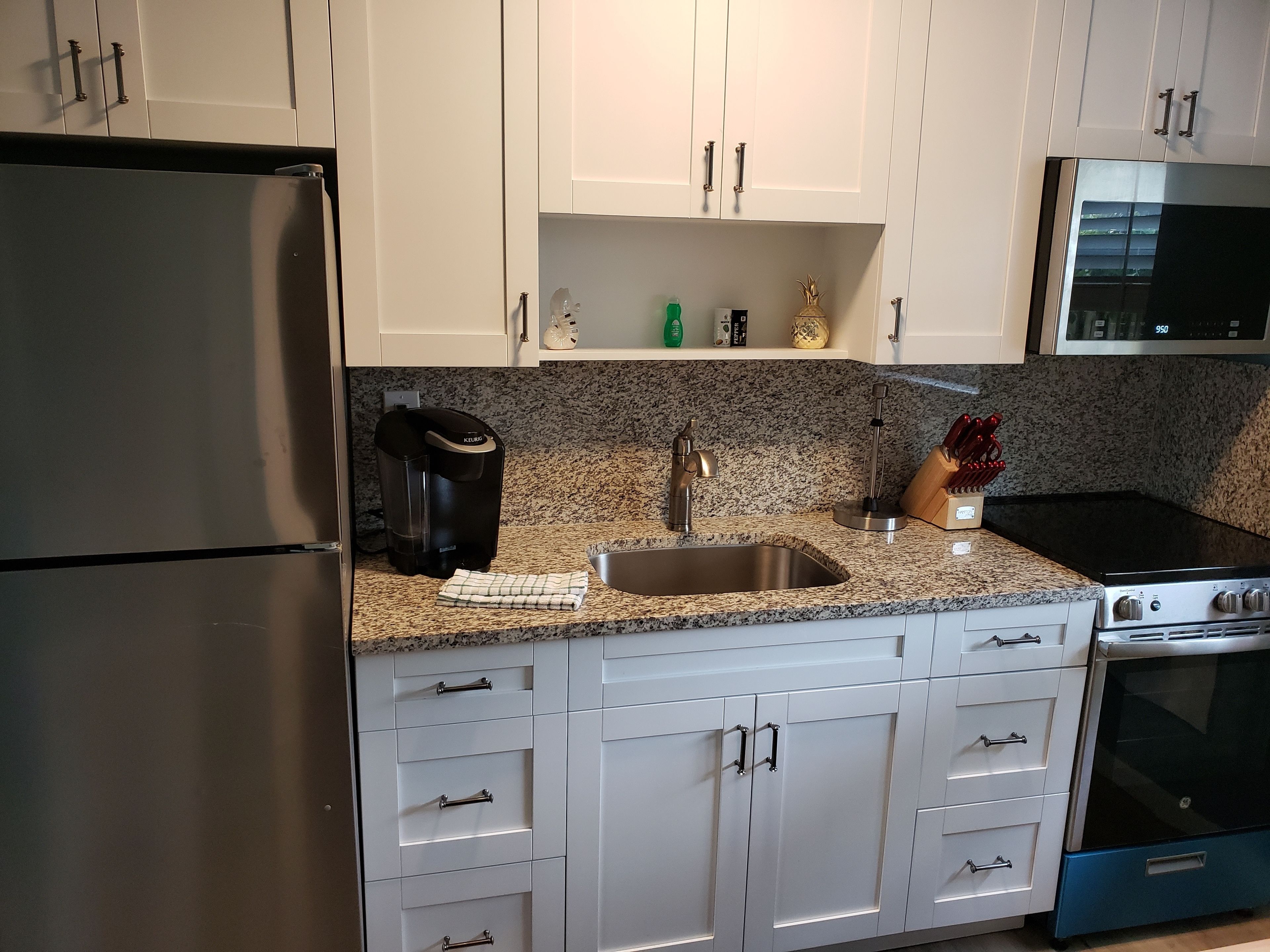 A kitchen with white cabinets, a stainless steel refrigerator, a coffee maker, a microwave, and a stove.