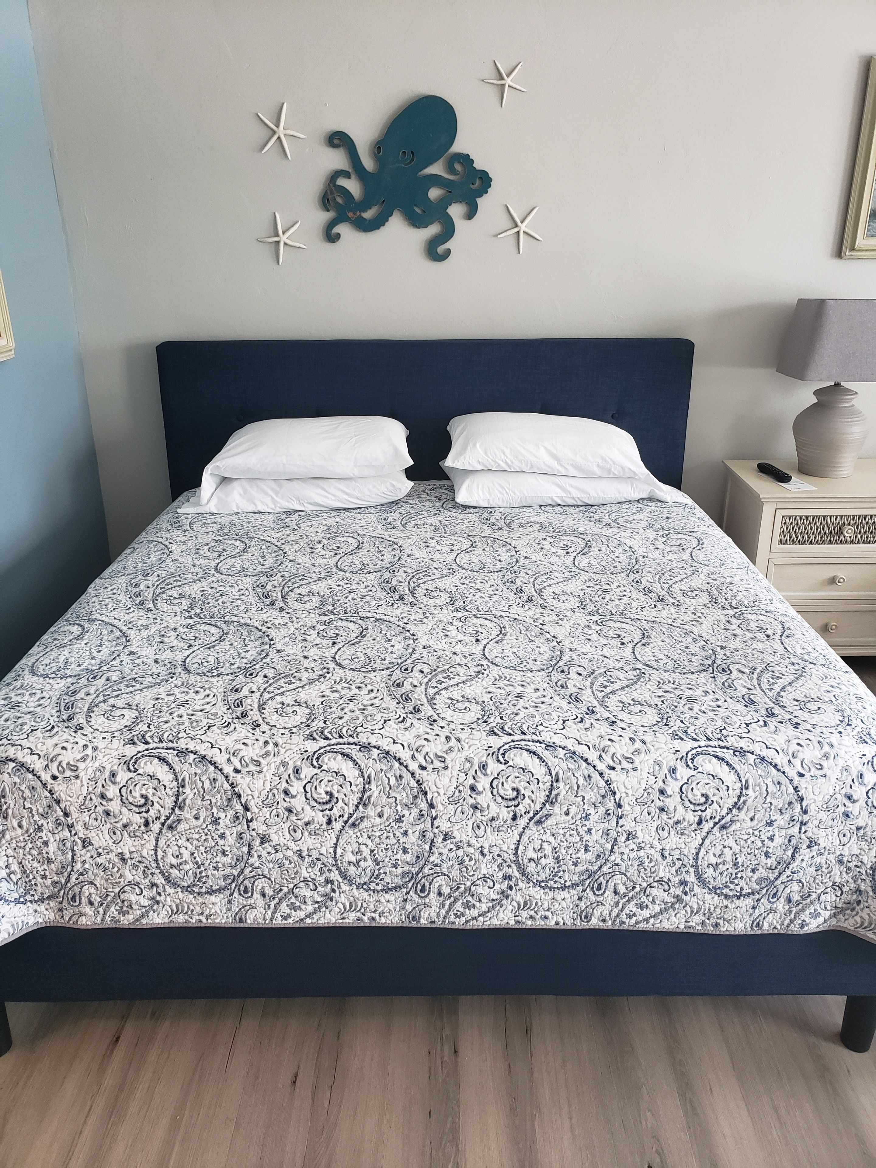 Uma cama com colcha estampada, cabeceira escura e decoração de polvo na parede.