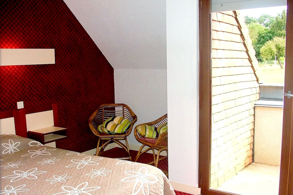 A bedroom with a bed, two wicker chairs, a small table, and a sliding glass door leading to an outdoor area.