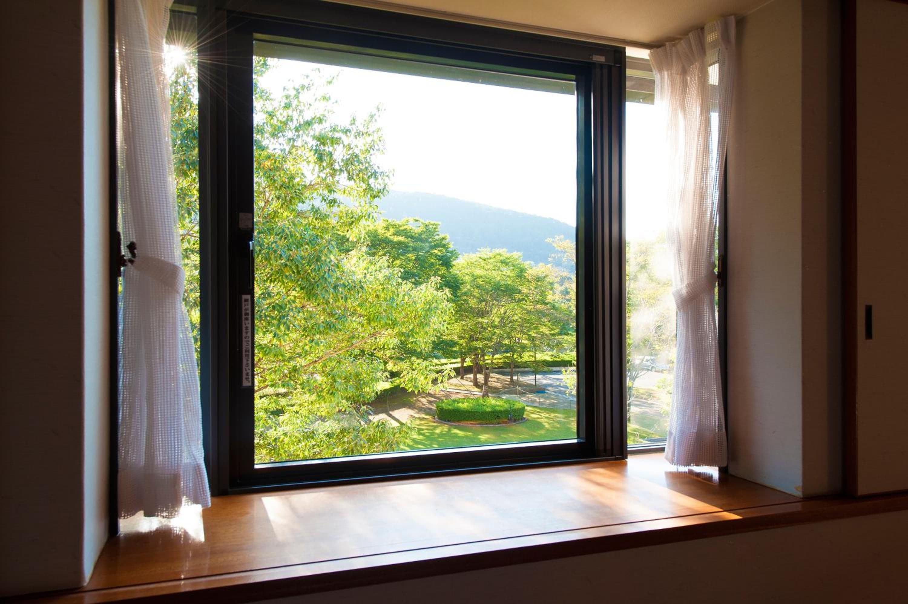 Quarto com uma grande porta de correr de vidro que dá para um jardim com árvores e um lago.