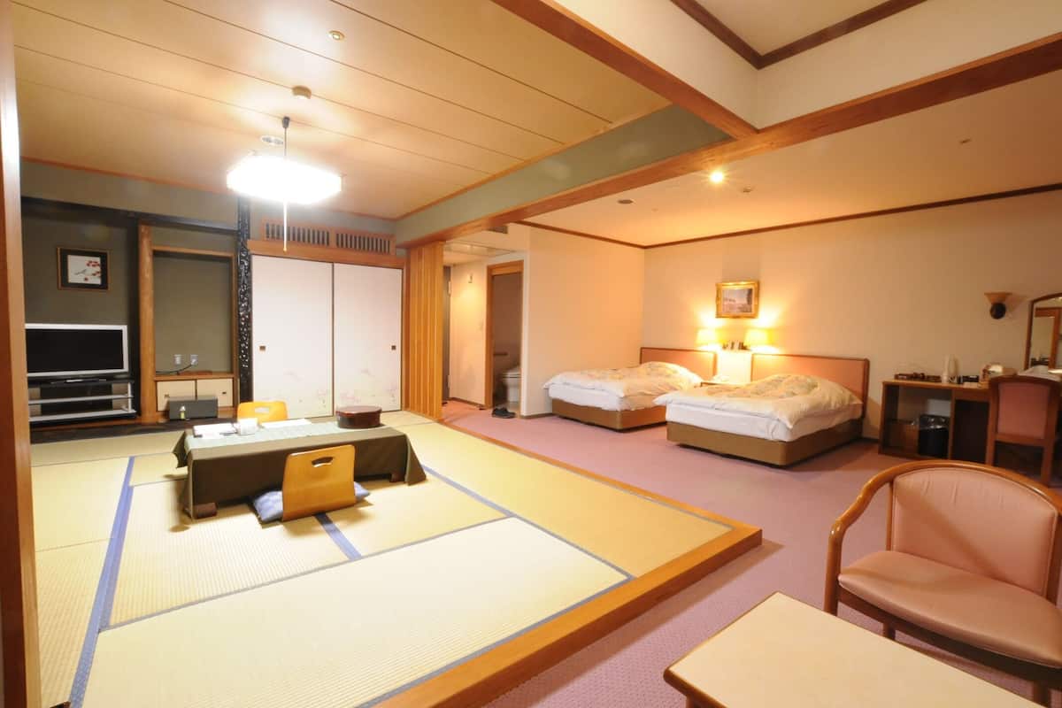 Una habitación tradicional japonesa con suelo de tatami, futón, escritorio y televisor.