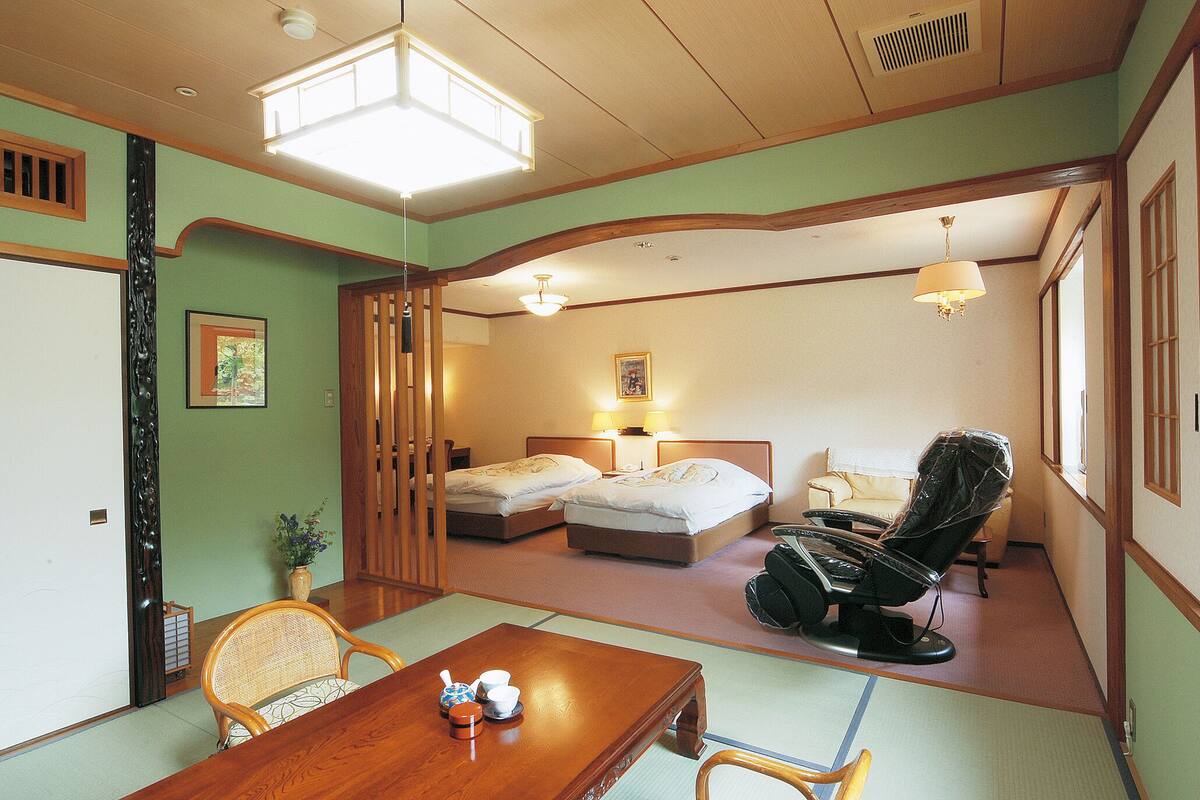 Una habitación tradicional japonesa con suelo de tatami, dos camas individuales, un sillón de masaje, una mesa de madera con tazas y una puerta corredera de shoji.