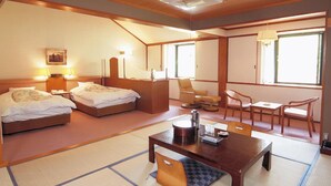 A traditional Japanese-style room with tatami flooring, two beds, a sitting area with a low table and chairs, and a large window providing natural light. - Watarase Onsen Hotel Sasayuri (Tanabe)