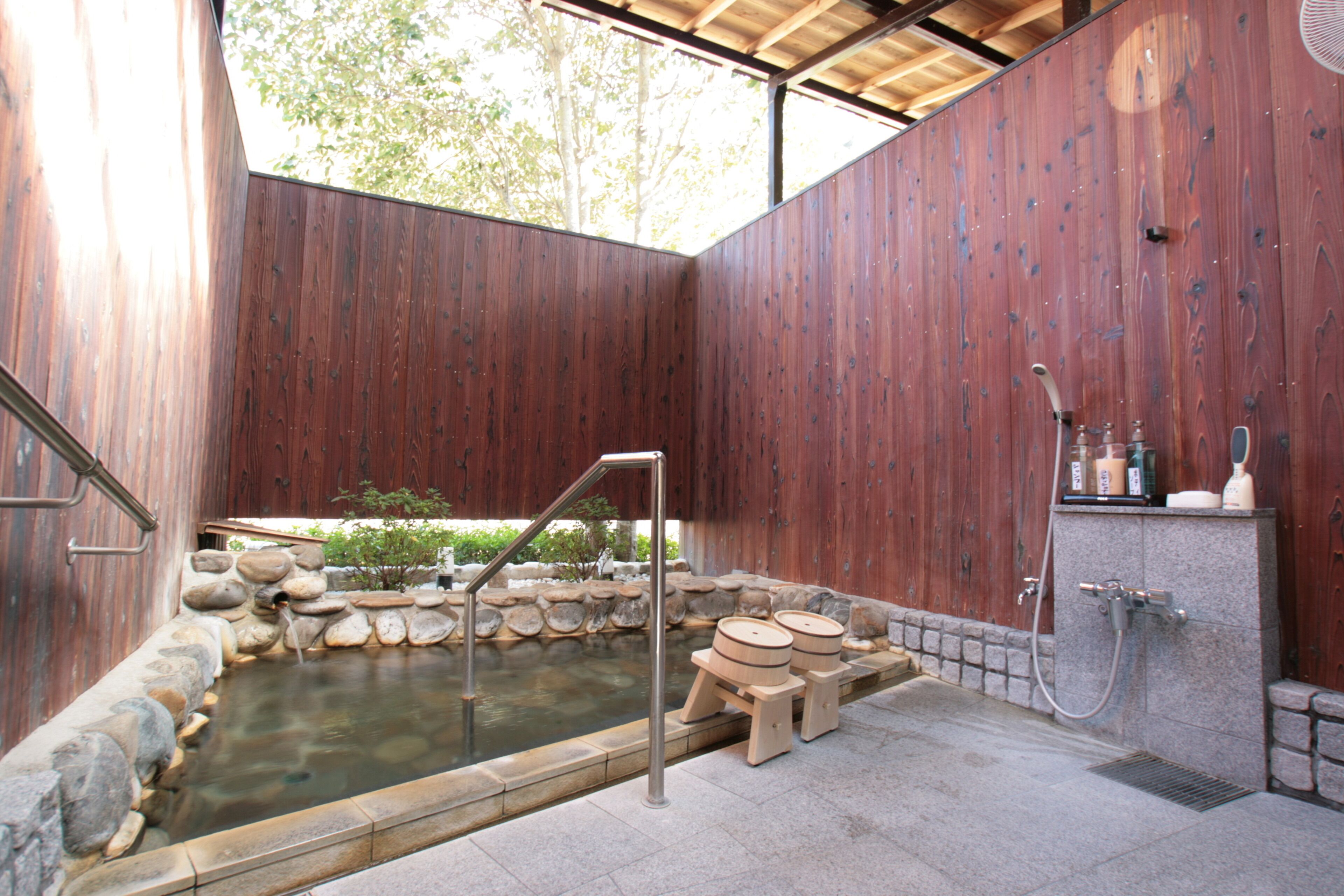 A wooden spa area with a hot spring, stone steps, and a shower.