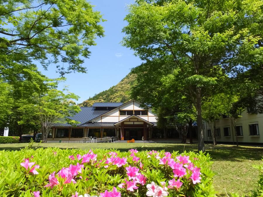 A traditional building with a sloped roof, surrounded by lush greenery and flowering plants.
