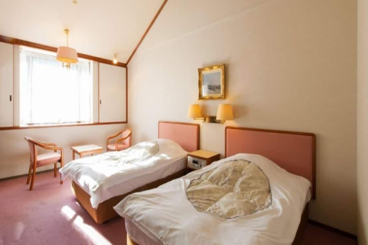Una habitación de hotel con dos camas, una silla, un escritorio y una ventana.