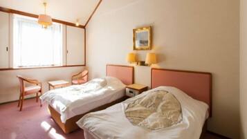 Quarto de hotel com duas camas, uma cadeira, uma escrivaninha e uma janela.
