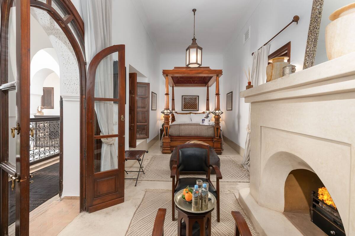 A room with a fireplace, a wooden bench, a table with bottles, and a hanging lantern.