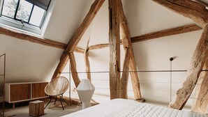 Een slaapkamer met zichtbare houten balken, een bed, een stoel en een nachtkastje.