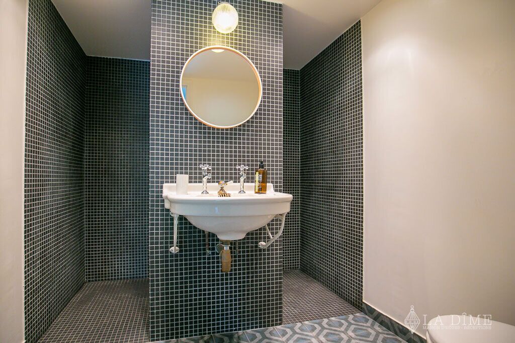 Un baño con un lavabo blanco, un espejo redondo y una lámpara de pared.