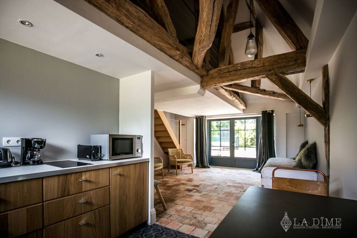 Una cocina moderna con vigas de madera, un comedor con sofá y una escalera que lleva a un balcón.