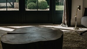 Een kamer met een groot raam, een houten tafel, een lamp en een bank.
