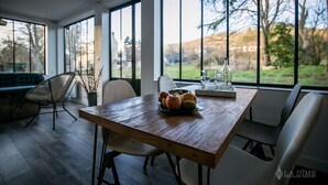Een eetruimte met een houten tafel, stoelen en een uitzicht op de omgeving door grote ramen.