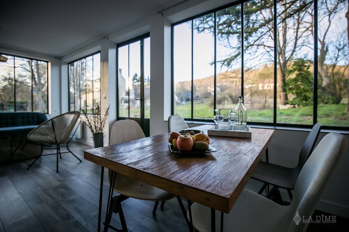 Un comedor con una mesa de madera, sillas y vistas al exterior a través de amplios ventanales.